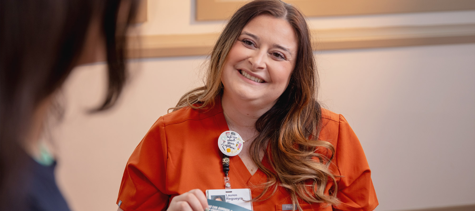 Healthcare worker in orange scrubs holding and pointing to a pamphlet.