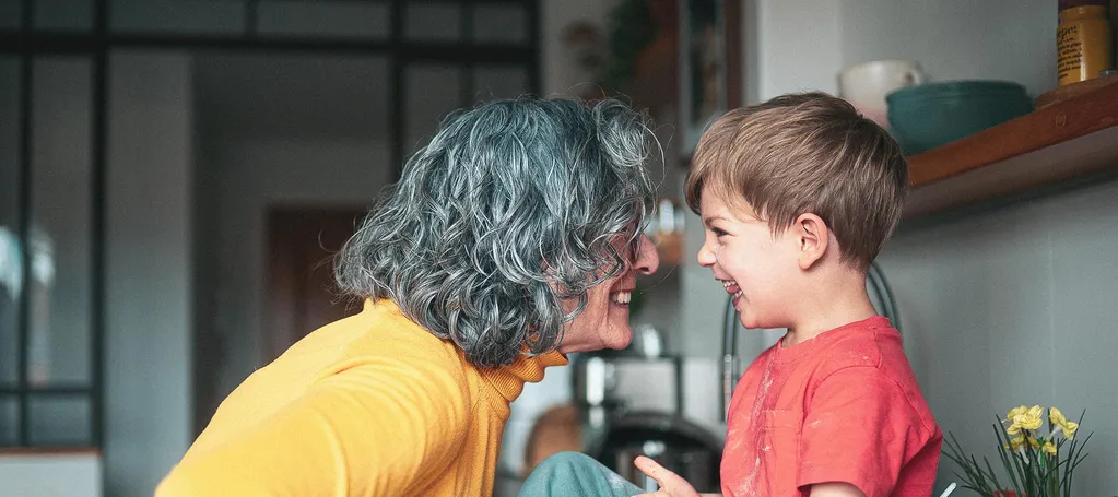 An older woman and a young child smile at each other while baking together in a kitchen.