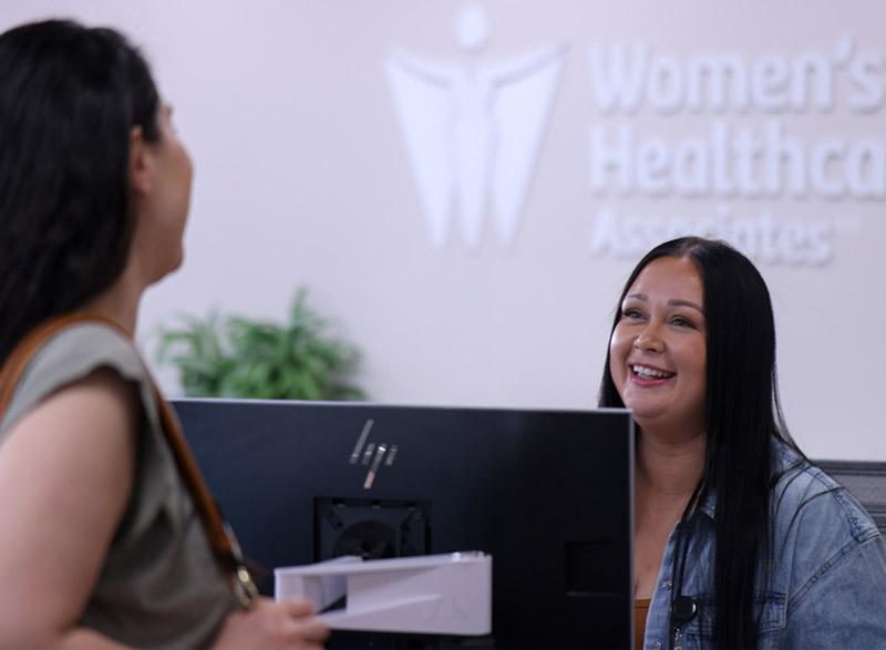 A patient services team member smiles while helping a patient at the front desk check-in counter.