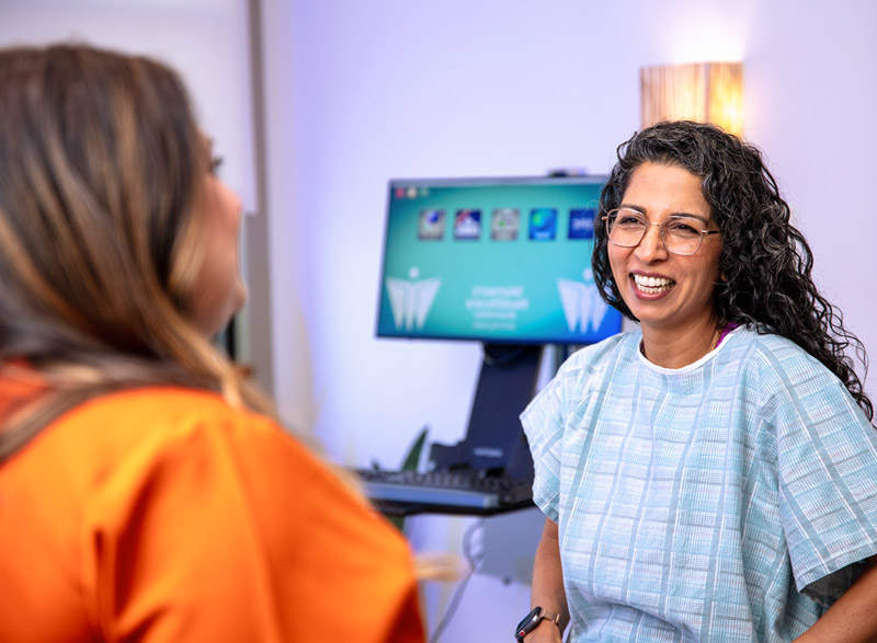 A patient in a gown smiles while talking with a clinician during an office visit.