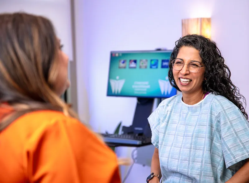 A patient in a gown smiles while talking with a clinician during an office visit.