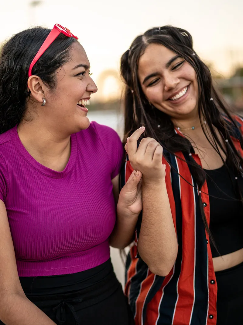 Two teenage girls laugh together while holding hands outdoors.