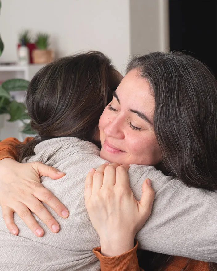 Two people share a comforting hug indoors, eyes closed in a calm moment.