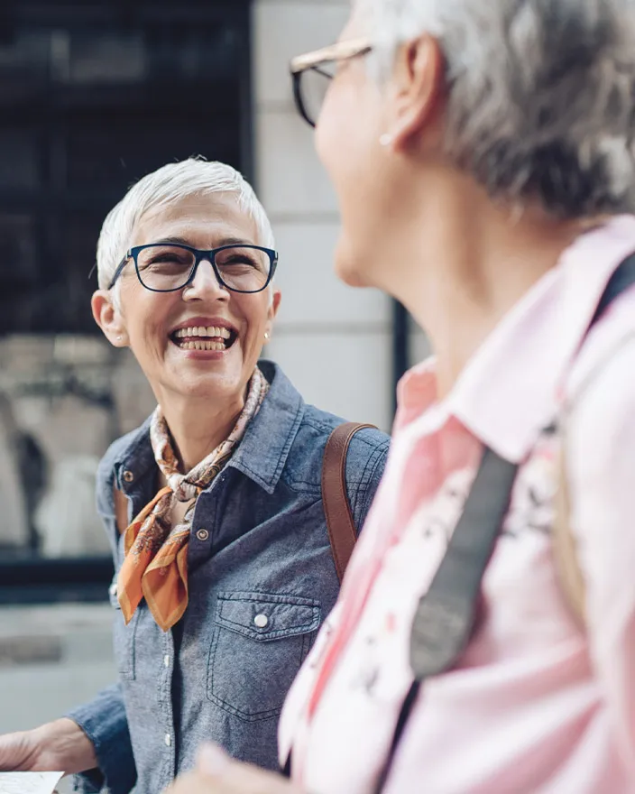Two older women walk together outside, smiling and chatting.
