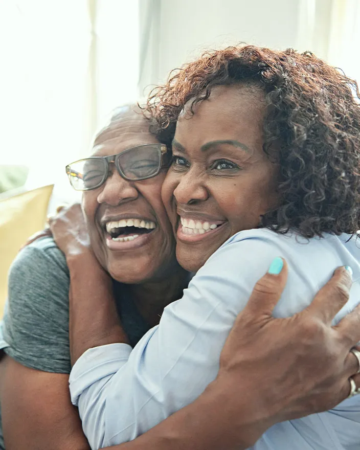 An older woman and a younger woman share a joyful hug, smiling broadly.