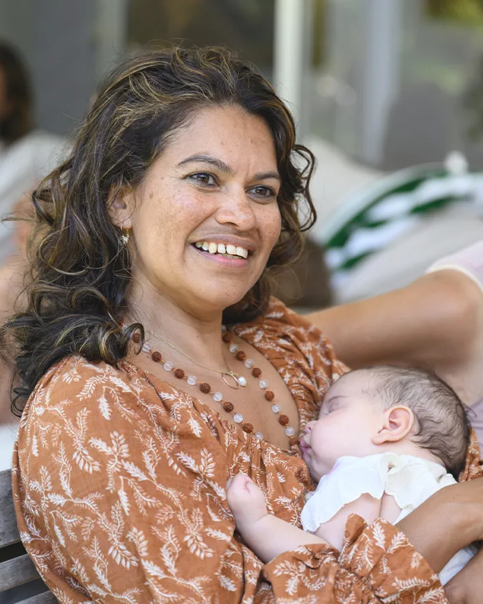 A woman cradles a sleeping baby while smiling gently.