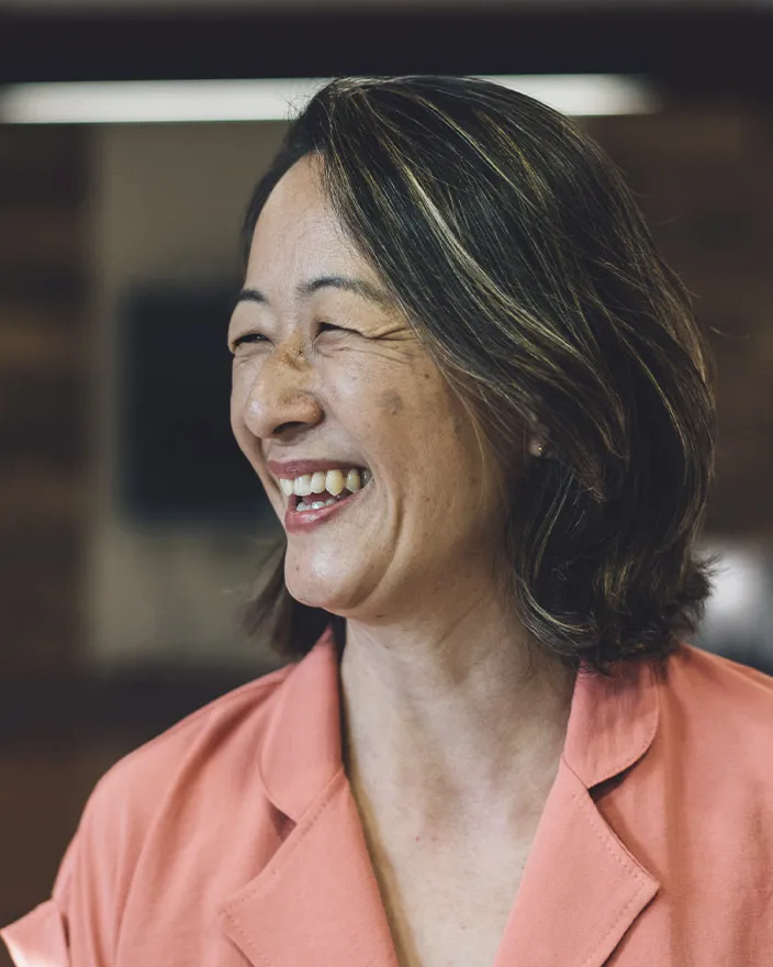 A woman laughs warmly, turned slightly to the side in a casual indoor setting.