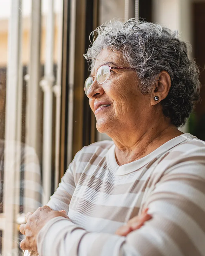 An older woman looks out a window with a calm, reflective expression.