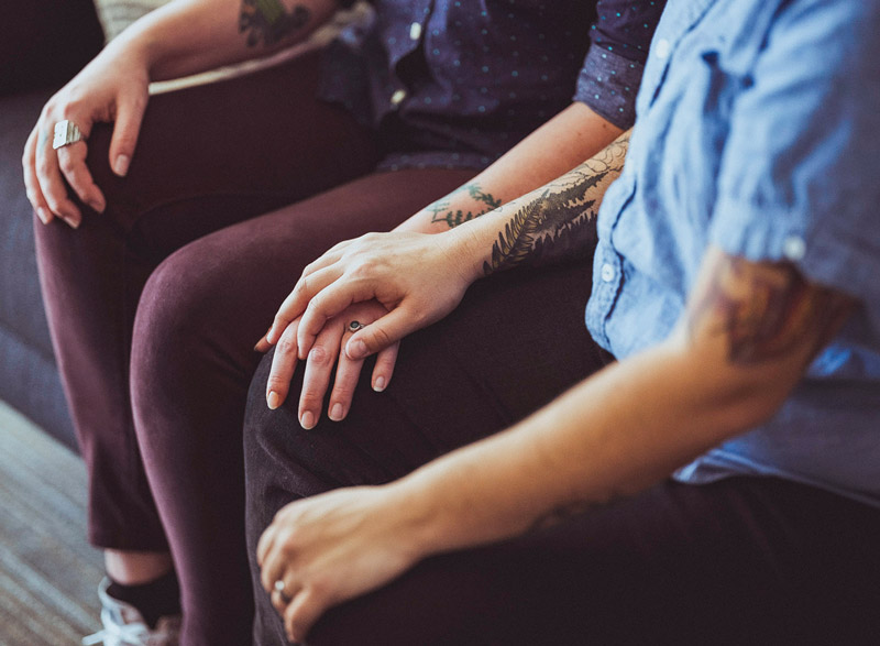 Close-up of two people seated side by side, one resting a hand on the other’s knee in a supportive gesture.