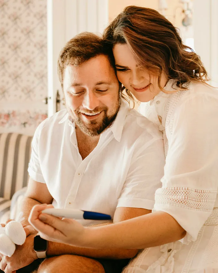 A couple smiling together while looking at a pregnancy test, appearing happy and excited.