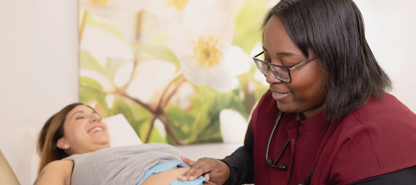Medical assistant performing a non-stress test on a smiling pregnant patient.