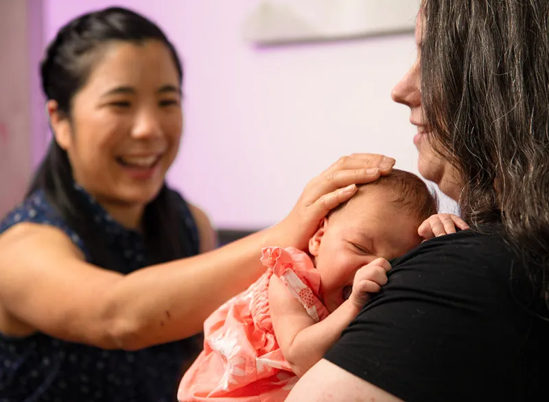 Mother holding newborn during postpartum clinic visit.