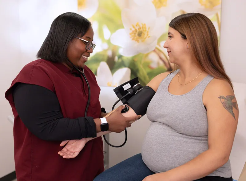Medical assistant checking pregnant patient blood pressure.